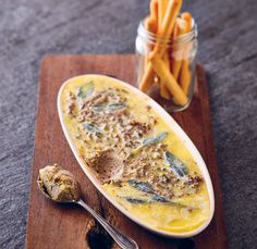 a wooden cutting board topped with food next to a jar of french fries and a spoon