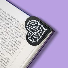 an open book with a spider web design on the front and back cover, sitting on a purple background