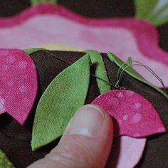 a person is stitching together some fabric with green and pink leaves on the side