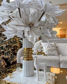 a white table topped with a vase filled with flowers next to a couch and christmas tree