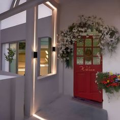 a red door and window with flowers on the outside, next to a white wall