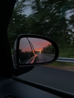 the rear view mirror of a car as it is driving down a road at sunset