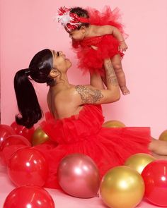 a woman in a red dress holding a baby up to her face while surrounded by balloons