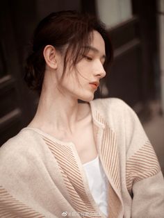 a woman with dark hair wearing a beige cardigan and white shirt is looking off to the side