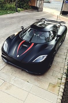 a black sports car with red stripes parked on the side of the road in front of a house