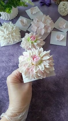 someone is holding up some paper flowers on top of a purple table with other items in the background