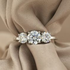 three stone diamond ring sitting on top of a cloth