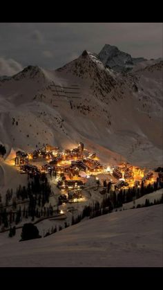 an image of a town in the mountains at night with lights on it's buildings