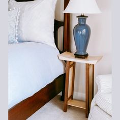 a blue vase sitting on top of a wooden table next to a bed with white sheets