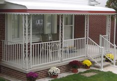 a porch with white railings and flower pots on the ground next to it, in front of a brick house