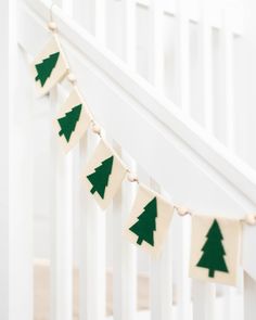 a garland with green christmas trees hanging from the side of a white crib in a nursery