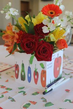 a vase filled with red roses and yellow flowers on top of a white table cloth