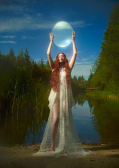 a woman with red hair holding a white frisbee over her head in front of a body of water