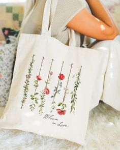 a woman sitting on the floor holding a white bag with red roses and leaves painted on it