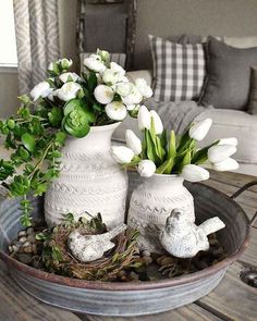 two white vases filled with flowers on top of a table next to a bird's nest