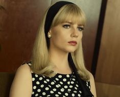 a woman with long blonde hair wearing a black and white polka dot dress sitting on a couch