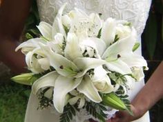 a bride holding a bouquet of white lilies in her hands and wearing a wedding dress