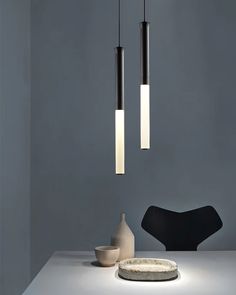 three lights hanging from the ceiling above a table with a bowl and vase on it