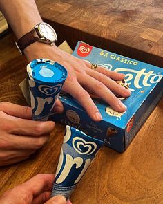 a person holding onto a blue and white toothpaste tube next to a box on a wooden table