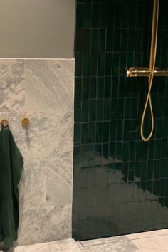 a bathroom with green tile and gold shower faucet next to the bathtub