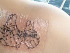 a tattoo on the back of a woman's shoulder shows two rabbits playing with a toy