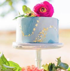 a blue and white cake sitting on top of a table with pink flowers around it