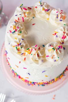 a cake with white frosting and sprinkles sitting on a pink plate