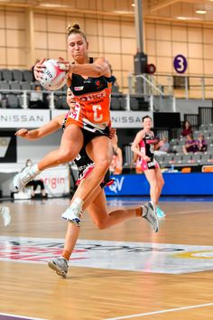 two women are playing basketball in an indoor court with people watching from the sidelines