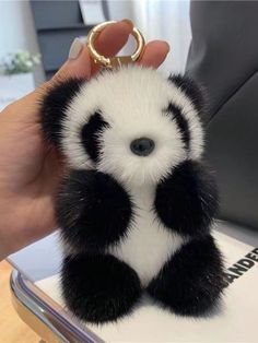 a hand holding a small black and white panda bear keychain on top of a table