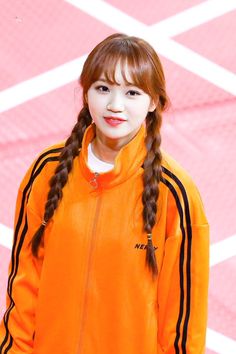 a girl with long hair wearing an orange jacket and standing in front of a pink wall