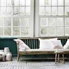 a wooden bench with pillows and vases on the floor in front of large windows