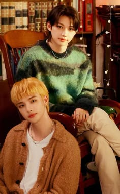 two young men sitting next to each other in front of a bookshelf filled with books