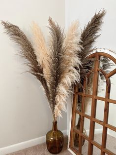 a vase with dried grass in it next to a mirror on the floor near a wall