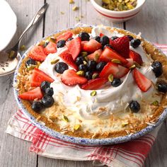 a pie topped with whipped cream and berries on top of a table next to bowls of fruit