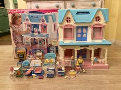 two dolls and toys sitting on the floor in front of a toy house with furniture