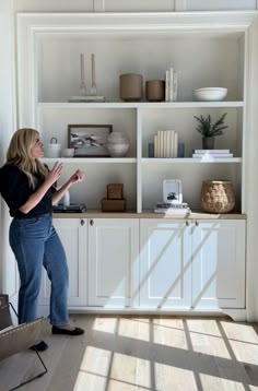 a woman standing in front of a white book shelf filled with books and vases