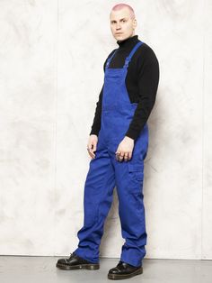 "Full and ready vintage 90's men work dungarees in indigo blue. Classic flap closure and durable fabric to accompany you on all kinds of works. Multiple front pockets. CONDITION: good vintage; has a spots here and there, see the last picture. MODEL is 6.4 ft (196 cm) tall, size XL - and he wears the size available. SIZE: Suggested size: L. To be sure the size will fit check the sizing details listed below. FLAT Measurements Side to side (waist): 16 1/2 \" / 42 cm Length: 51 \" / 129,5 cm Inseam: Blue Utility Jumpsuits And Rompers With Side Pockets, Blue Denim Jumpsuit With Side Pockets, Blue Utility Jumpsuits With Side Pockets, Blue Overalls With Pockets, Blue Utility Overalls With Bib Front, Blue Overalls With Pockets For Streetwear, Blue Shortalls With Pockets, Blue Cotton Utility Shortalls, Blue Workwear Overalls