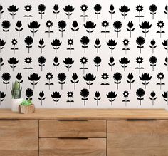 black and white flowers on a wall next to a wooden dresser with a potted plant