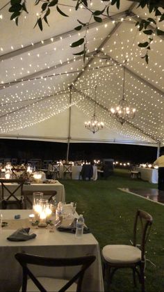 an outdoor tent with tables and chairs set up for a wedding reception under the lights