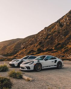 two white sports cars parked next to each other in front of a large mountain range