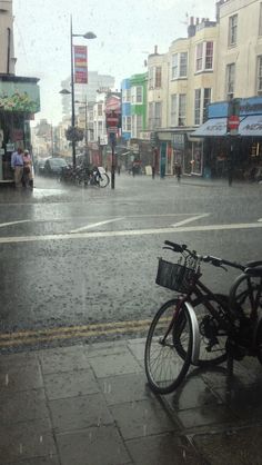 a bicycle parked on the side of a wet street next to a sidewalk with buildings in the background