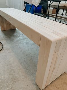 a wooden bench sitting on top of a hard wood floor next to a blue trash can