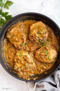 chicken with sauce in a skillet next to parsley on a white counter top