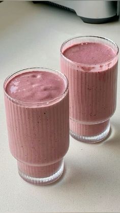 two glasses filled with pink smoothie sitting on top of a table