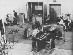 an old black and white photo of some people in a room with guitars, keyboards and other musical equipment