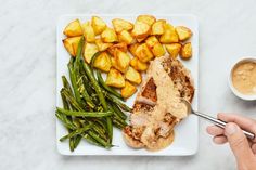 a person is holding a spoon over a plate of food with potatoes and green beans