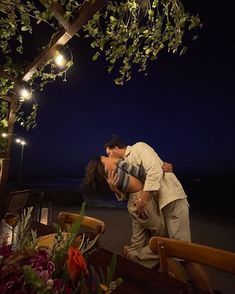 a man and woman kissing under an arbor with lights on the beach in the background