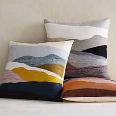 two decorative pillows sitting on top of a bed next to each other, one is multicolored