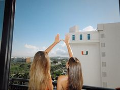 two women standing on top of a balcony with their hands in the air