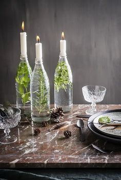 a table topped with bottles filled with plants next to plates and glasses on top of it